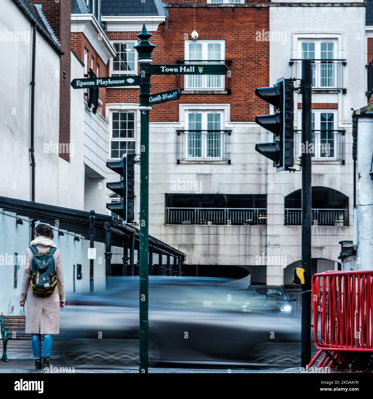 Epsom, Surrey, Londra, Regno Unito, novembre 20 2022, Donna in attesa da sola al semaforo di attraversare la strada con un vago auto che passa Foto Stock