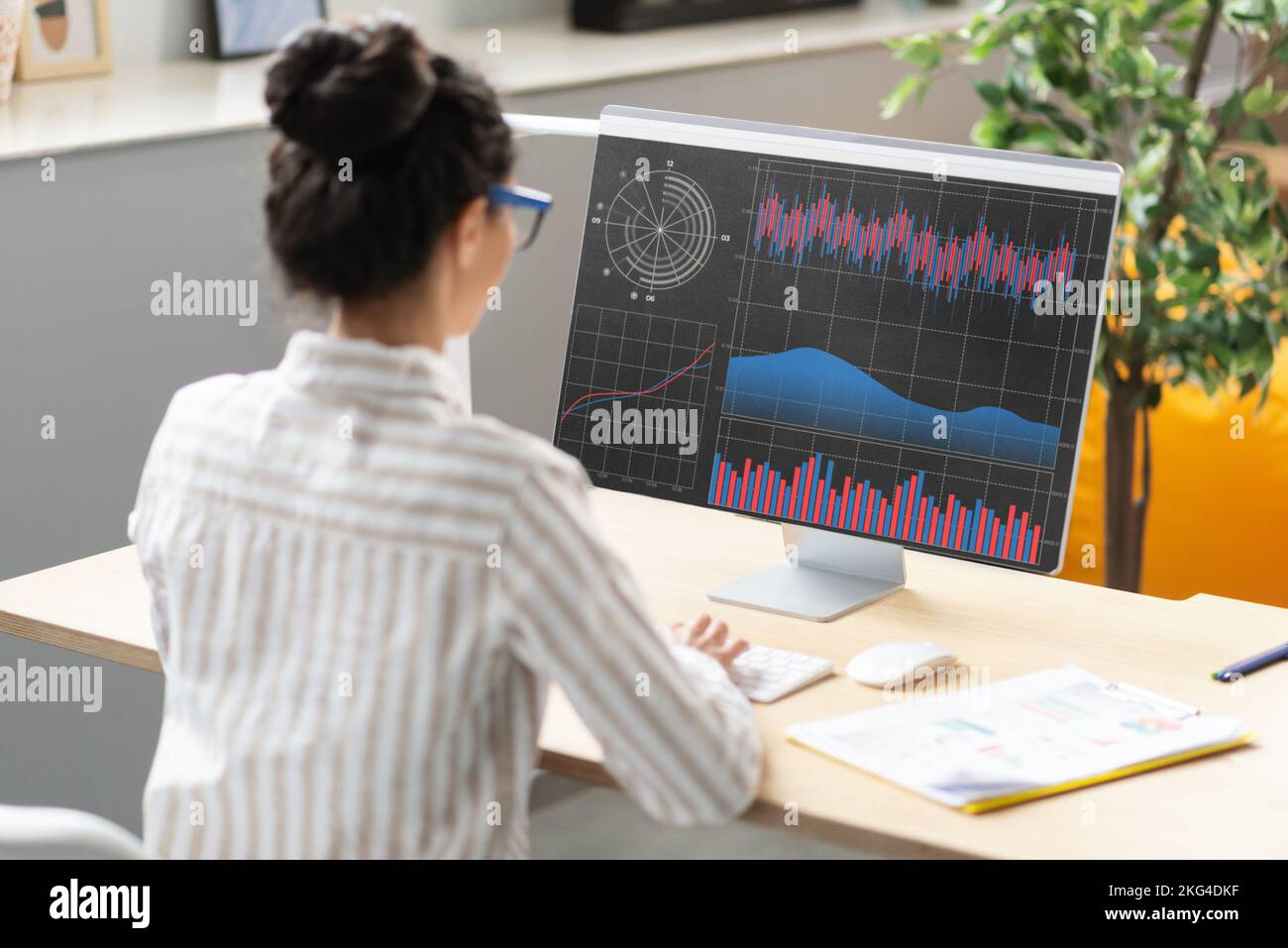 Giovane donna d'affari che analizza le statistiche sullo schermo del computer, lavorando con grafici finanziari e grafici online in ufficio Foto Stock