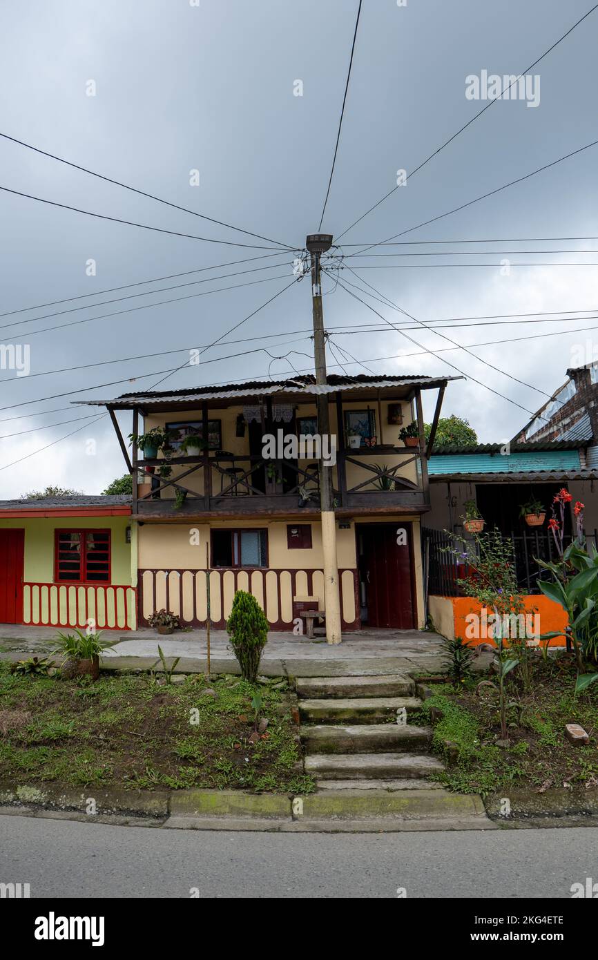Filandia, Quindio, Colombia - Giugno 5 2022: Palo di metallo di fronte ad una piccola Casa YellowColonial con un lotto di cavi distribuiti su lati diversi Foto Stock