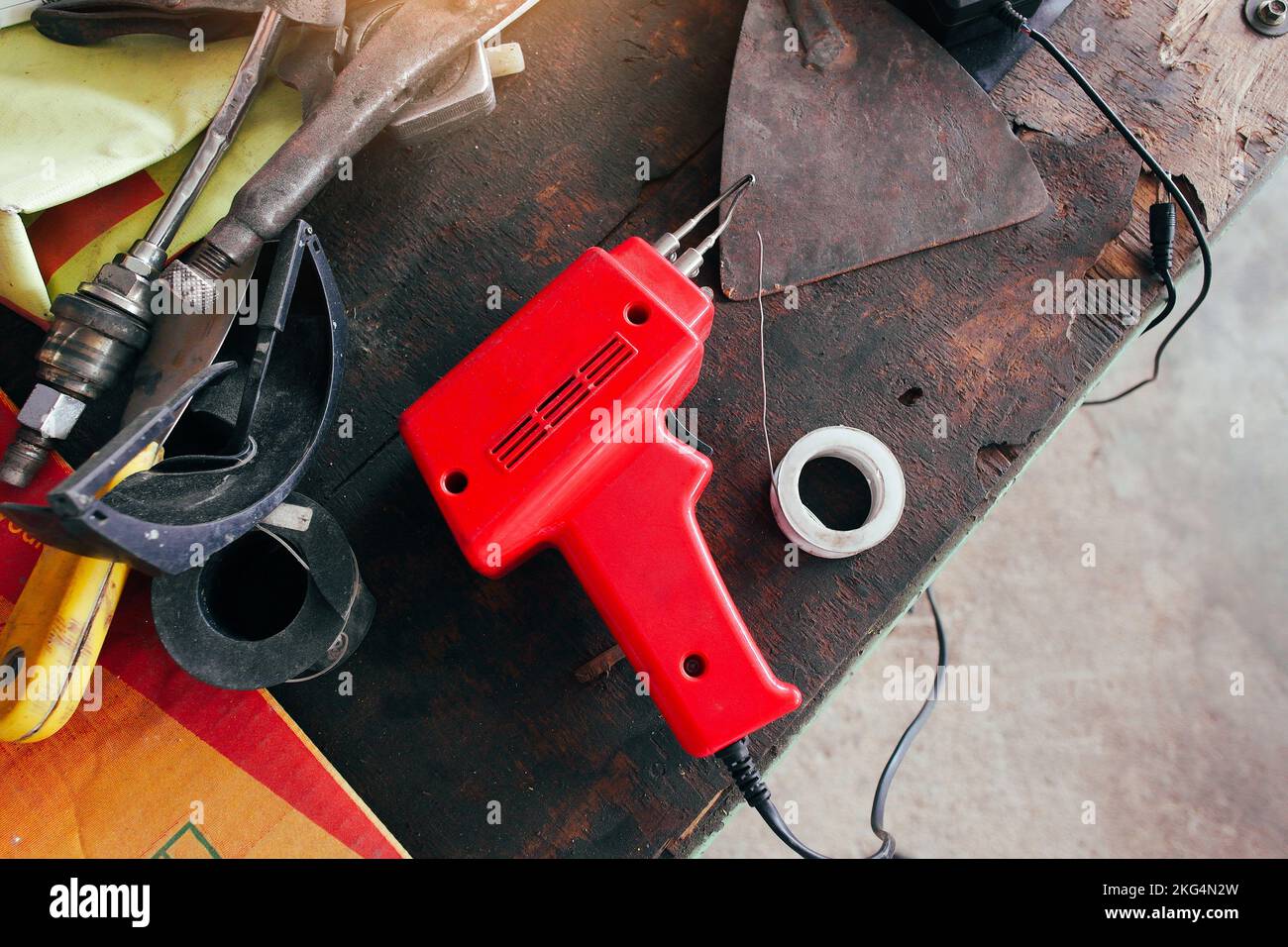 Saldatore elettrico rosso con piombo su un vecchio tavolo meccanico in legno. Foto Stock