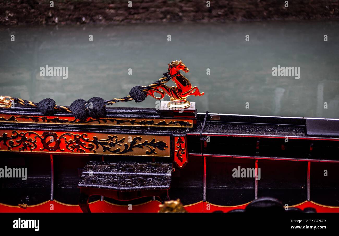 Un suggestivo ornamento in ottone a cavallo d'acqua sul lato di una gondola in legno con il rossore della vernice riflesso nel disegno. Foto Stock