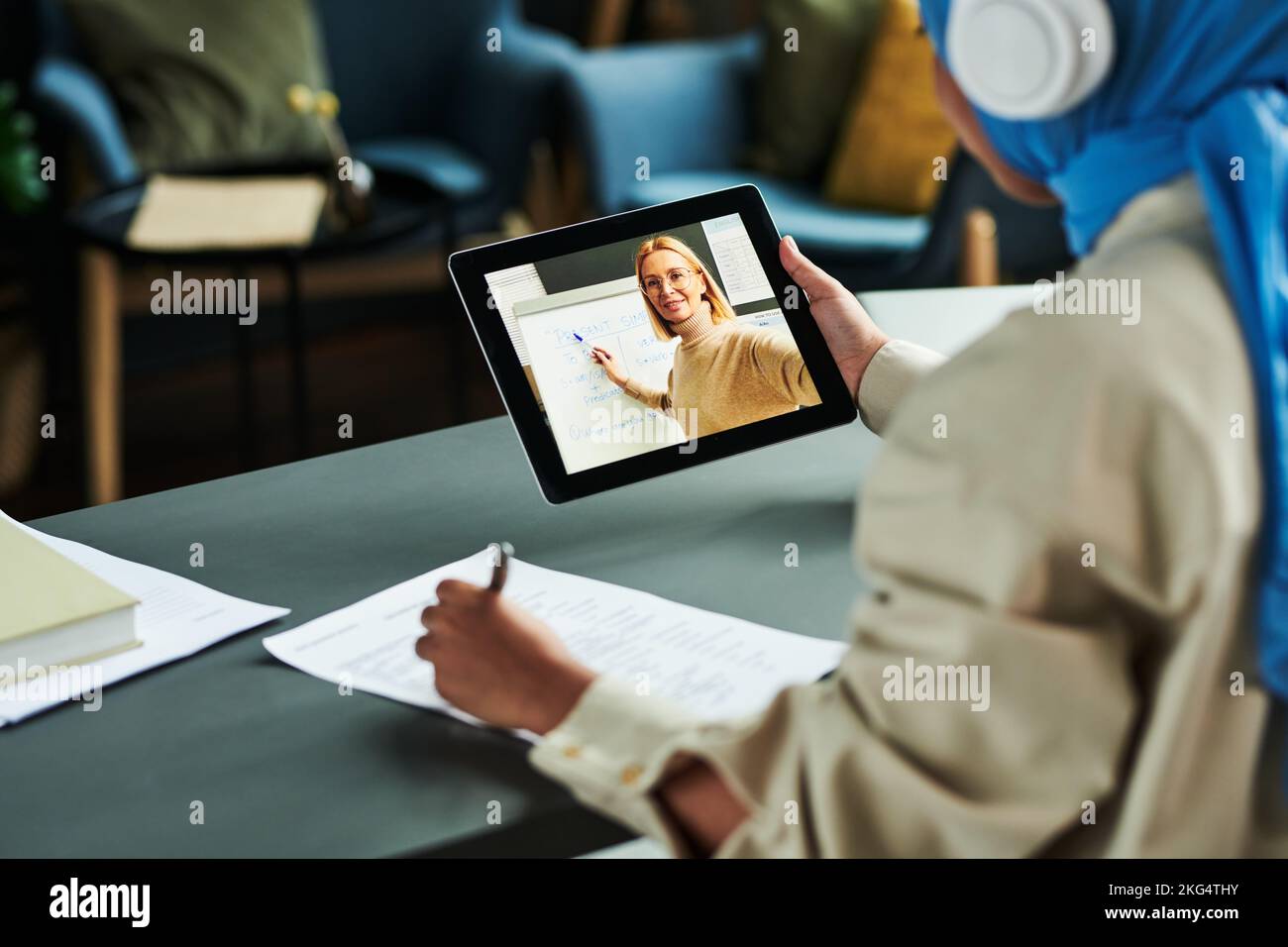Concentratevi sullo schermo del tablet con un insegnante fidato e biondo che indica la lavagna durante la spiegazione della grammatica inglese al pubblico online Foto Stock