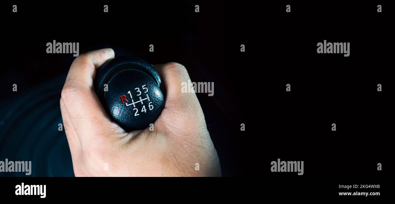 La mano del conducente sta cambiando le marce di un cambio manuale a 6 marce, banner panoramico con spazio di copia su sfondo nero Foto Stock