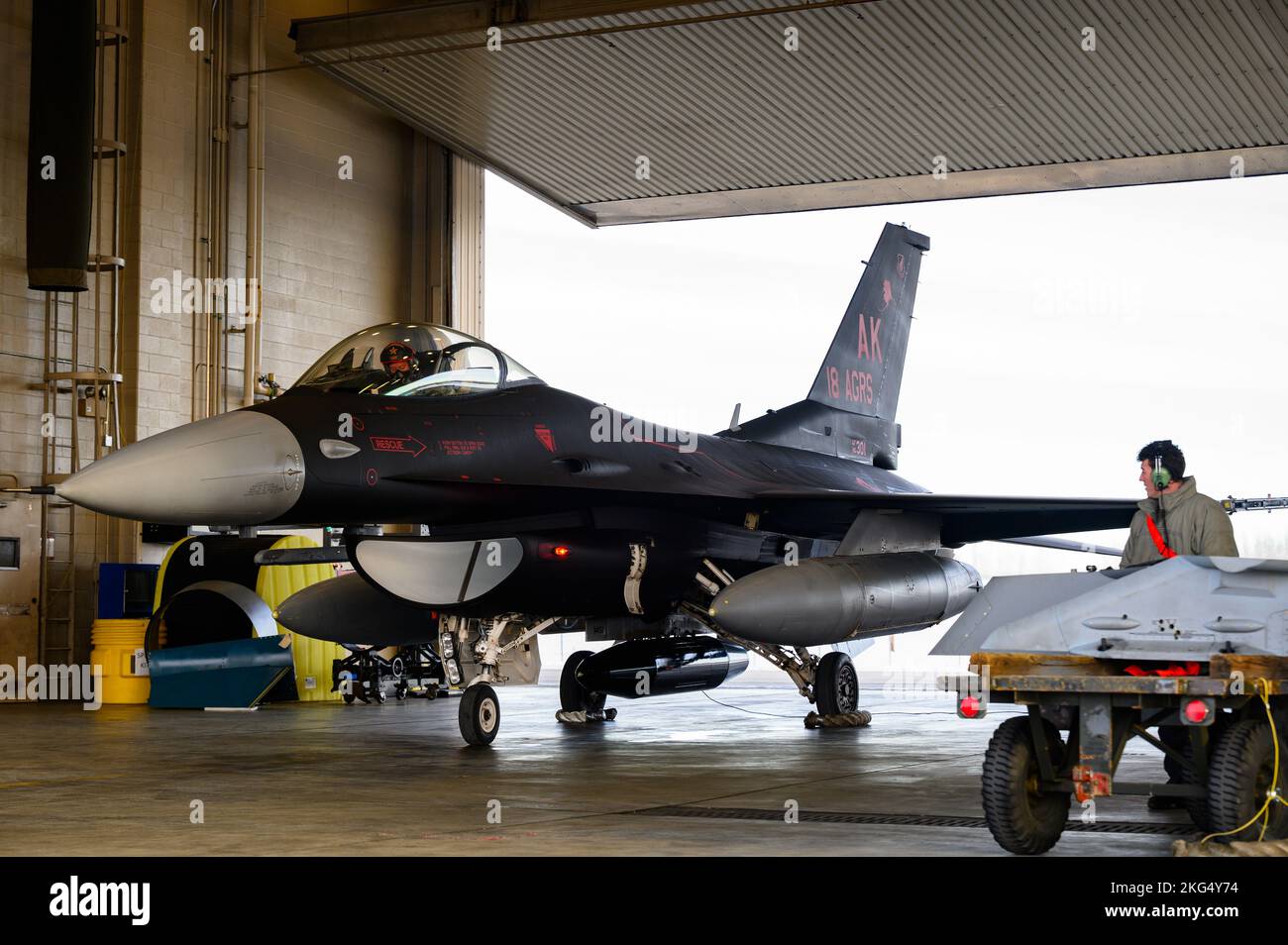 Un capo dell'equipaggio dell'aeronautica degli Stati Uniti assegnato all'unità di manutenzione dell'aeromobile 18th esegue operazioni di recupero su uno squadrone Aggressor 18th F-16 Fighting Falcon presso la base dell'aeronautica militare di Eielson, Alaska, 29 ottobre 2022. Questa è la prima volta che Eielson avrà lo schema di verniciatura dell'aggressore di wraith nel suo inventario aereo. Foto Stock