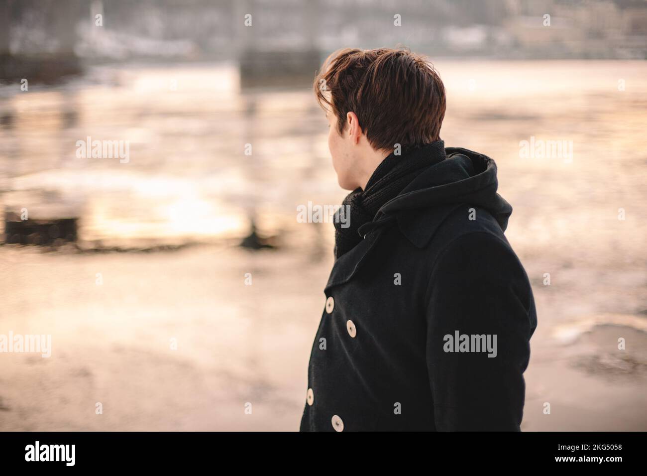 Ragazzo adolescente che indossa un cappotto e una sciarpa che guarda sul fiume mentre si trova all'aperto in inverno Foto Stock