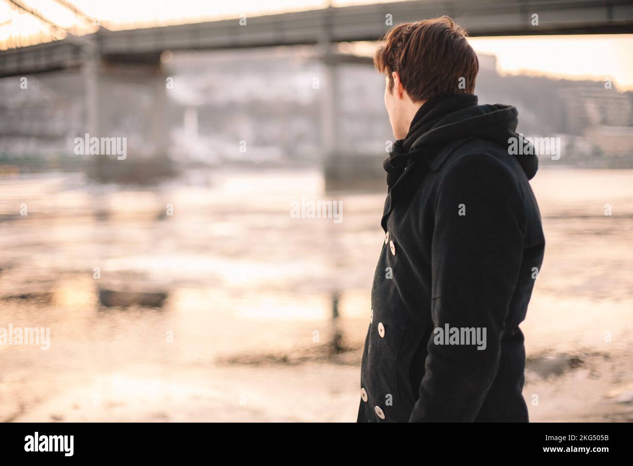 Giovane uomo che indossa cappotto e sciarpa che guarda sul fiume mentre si trova all'aperto in inverno Foto Stock