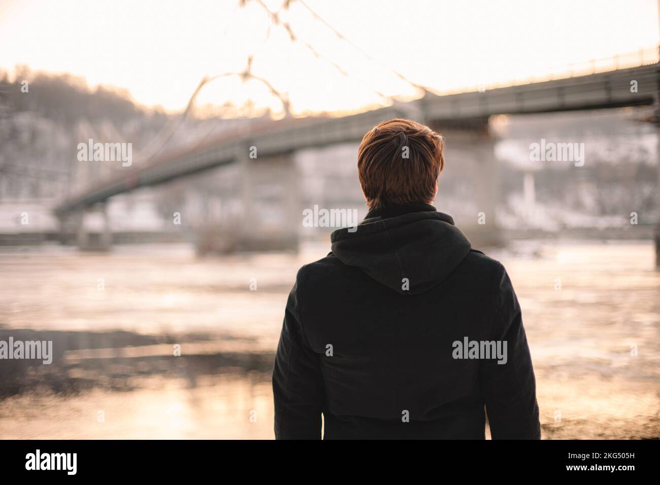 Vista posteriore di un giovane pensieroso che guarda il fiume mentre si trova all'aperto in inverno Foto Stock