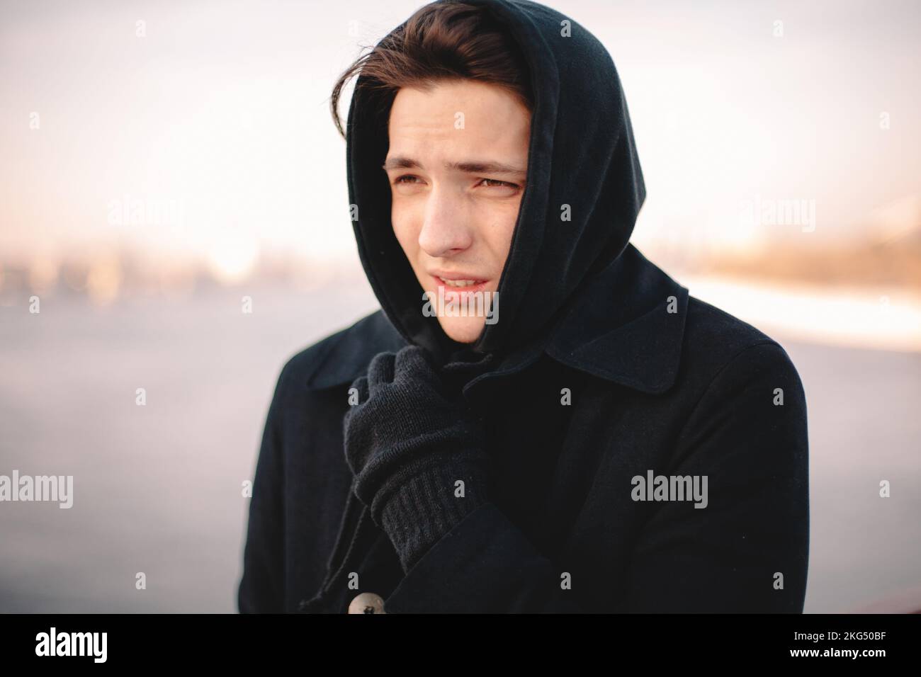 Ragazzo adolescente sensazione di freddo mentre in piedi all'aperto indossando il cappuccio in inverno Foto Stock