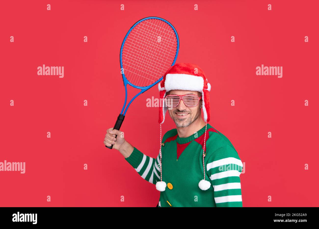 Buon Natale. felice uomo in costume di elfo e cappello di babbo natale. il ragazzo di natale tiene il razzo di tennis Foto Stock