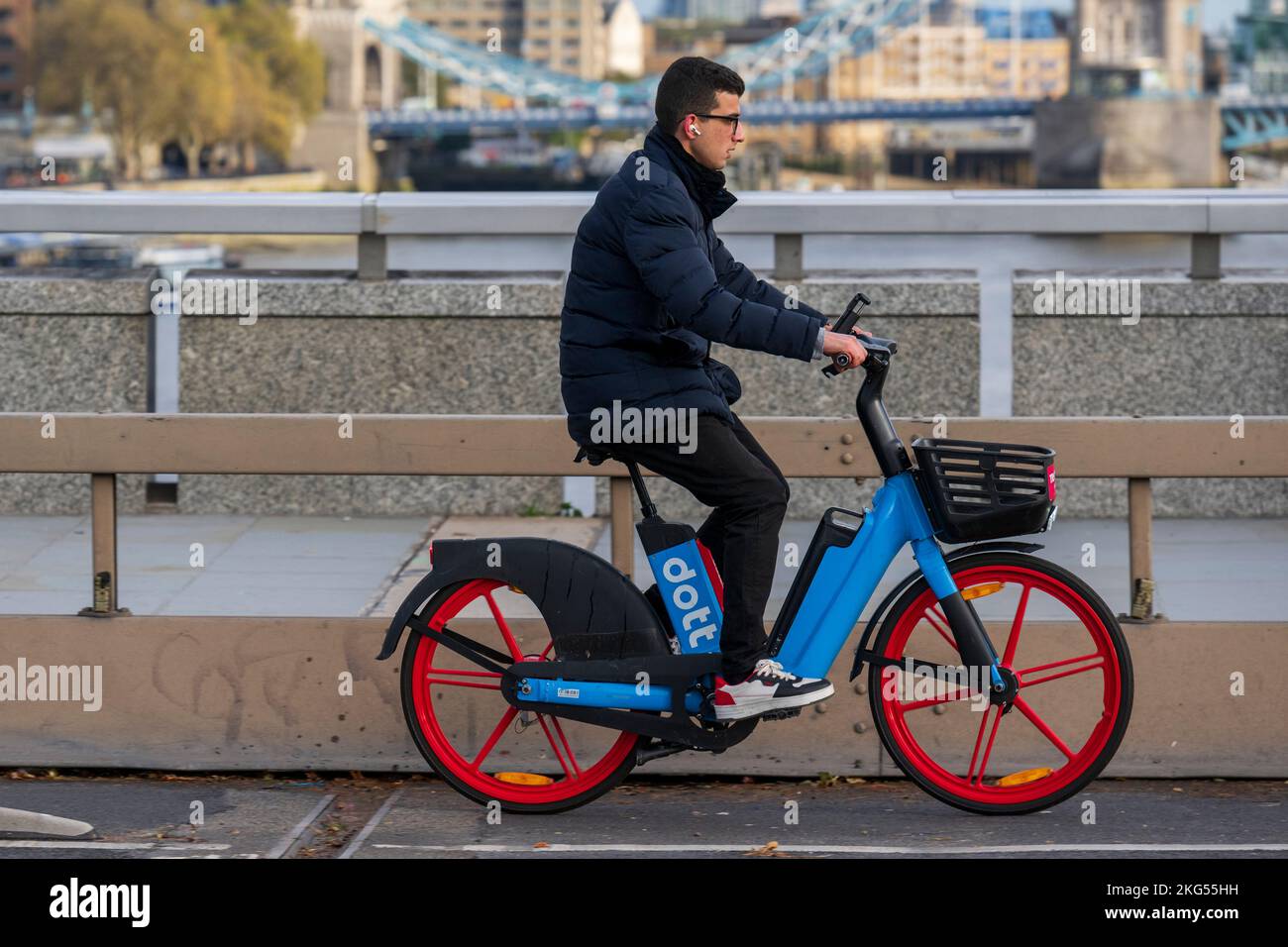 Un uomo che si mette in viaggio con una bicicletta elettrica a noleggio dott lungo il London Bridge durante l'ora di punta. London Bridge, Londra, Regno Unito. 17 Nov 2022 Foto Stock