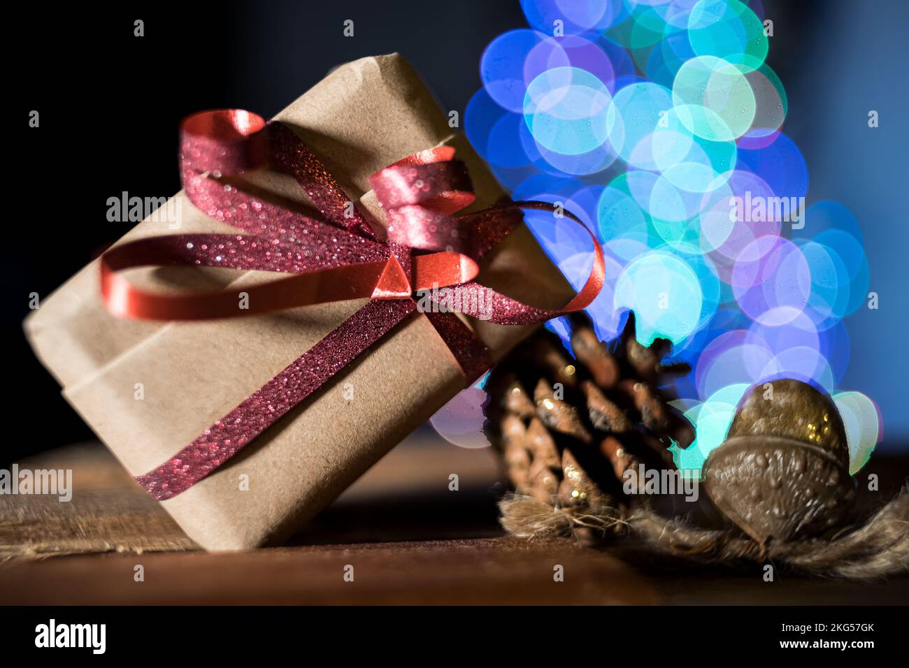 Immagine sfocata dell'albero di Natale illuminato contro sfondo nero. Regalo sostenibile in primo piano Foto Stock