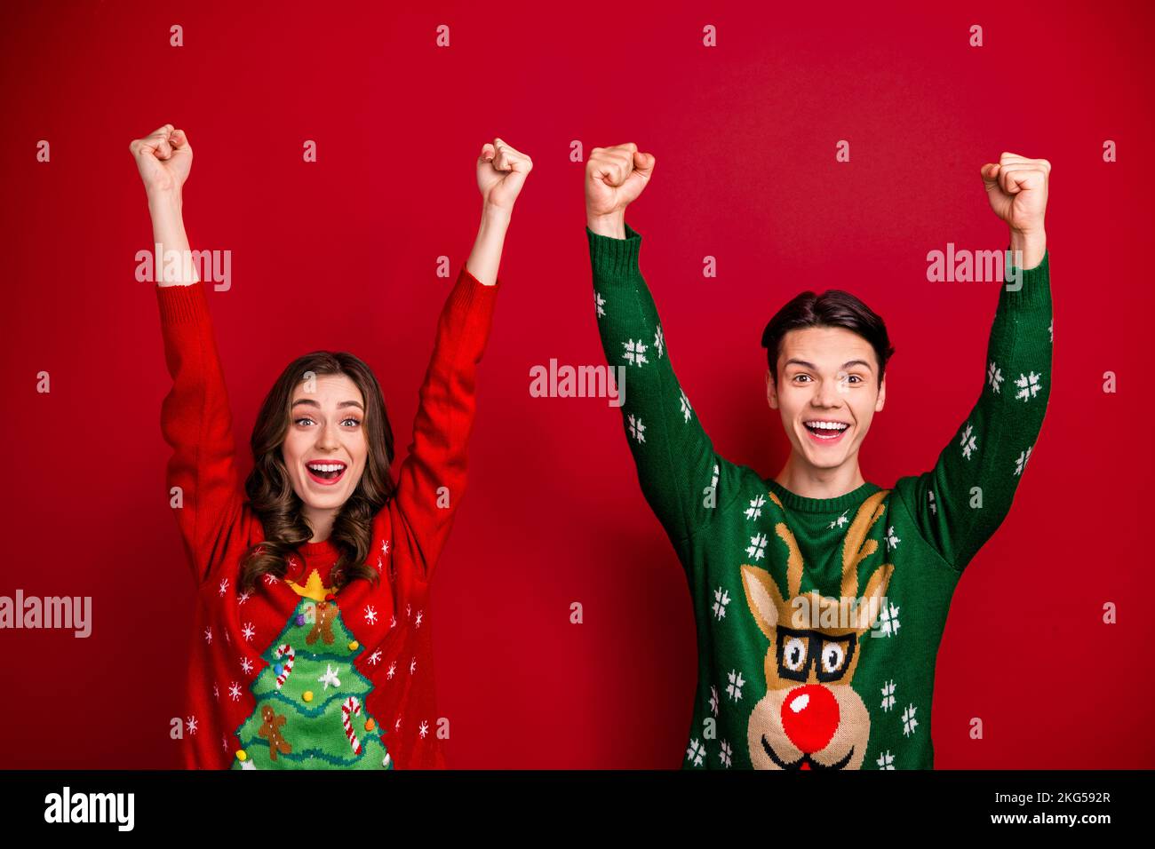 Foto di famiglia allegro fratello sorella brutto jumper sollevare le mani felice trionfo vittoria concorso lavoro aziendale isolato su sfondo di colore rosso Foto Stock