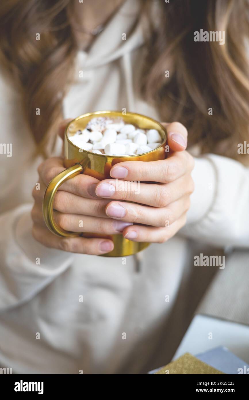 Closeup mani femminili che tengono la tazza dorata di lusso piena di marshmallow cacao Natale atmosfera Foto Stock