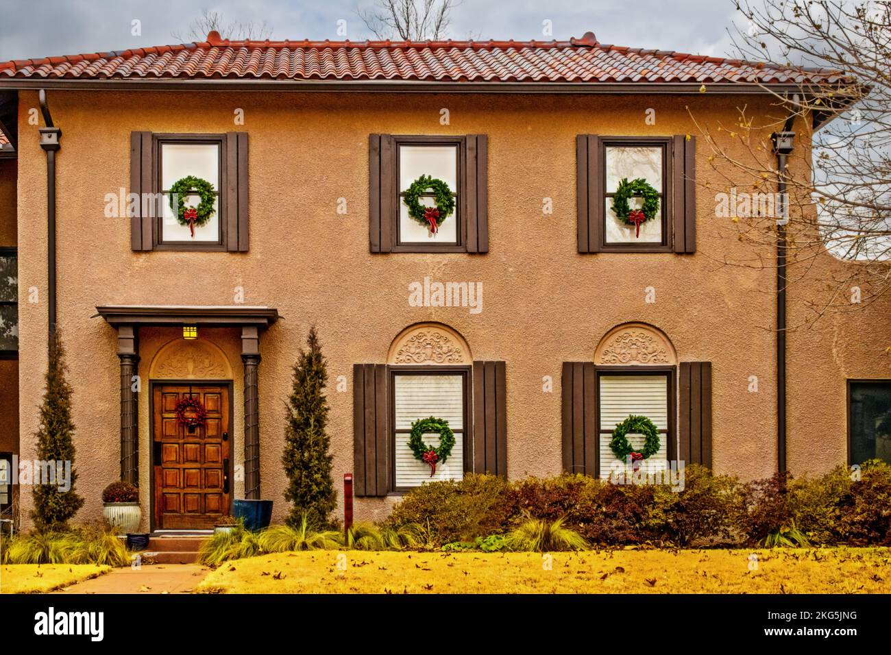 Stucco casa a due piani con tetto piastrellato decorato per Natale con corone in tutte le finestre Foto Stock