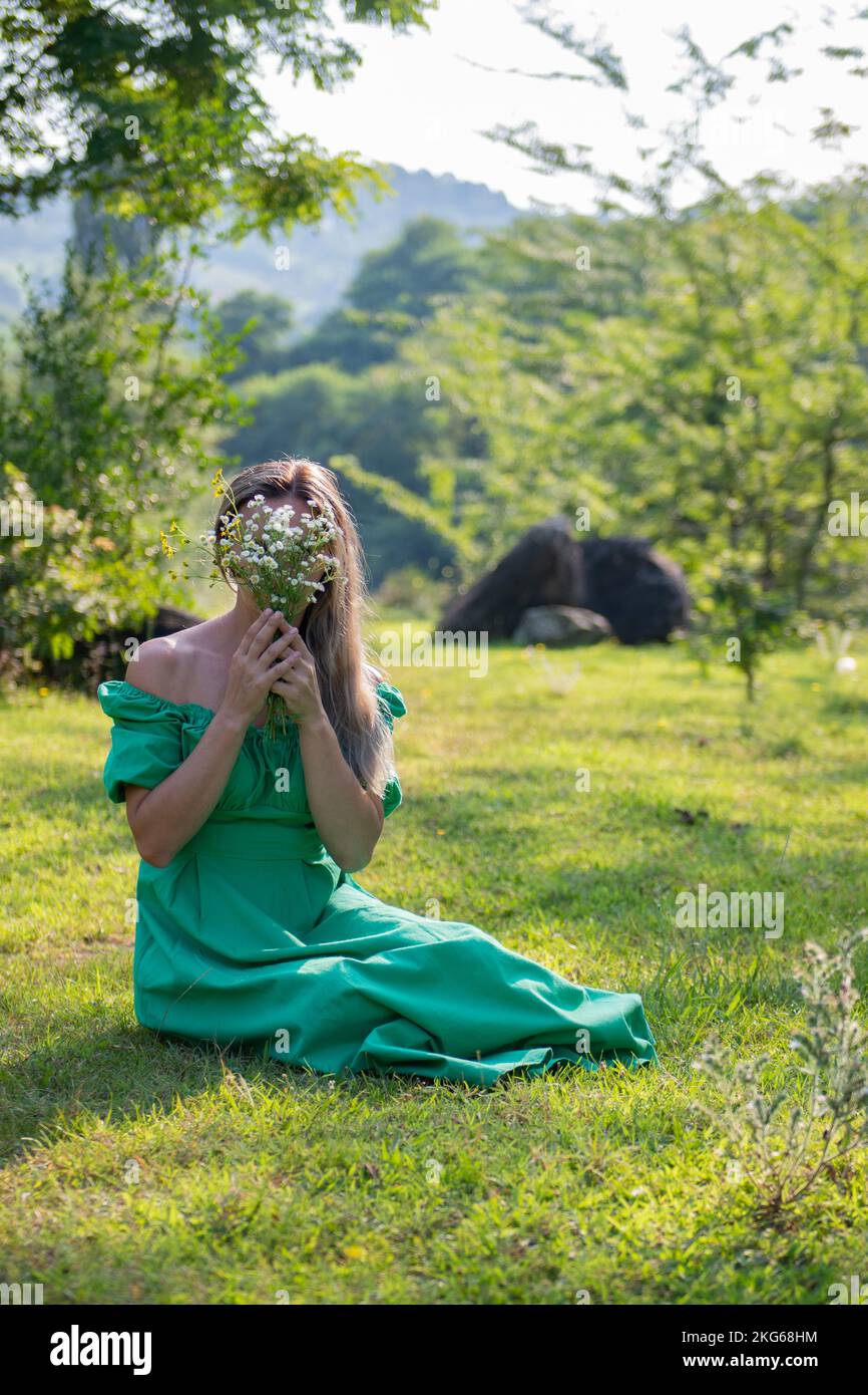 una ragazza è seduta sull'erba con i fiori in un vestito verde Foto Stock