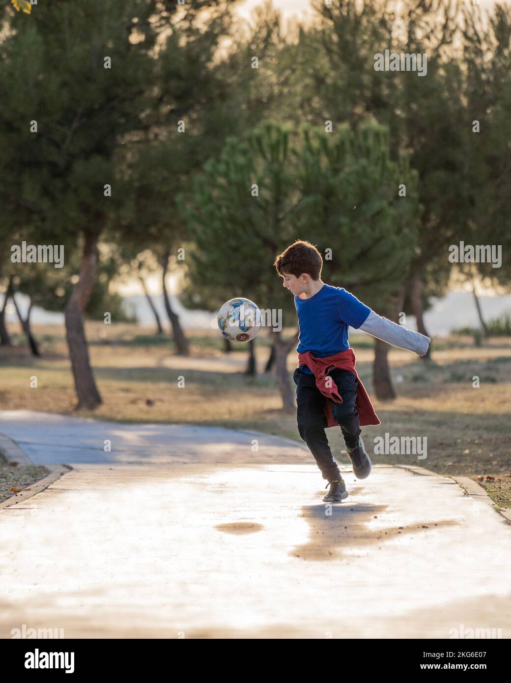 Ragazzo che gioca a calcio da solo in un parco naturale con ombre Foto Stock