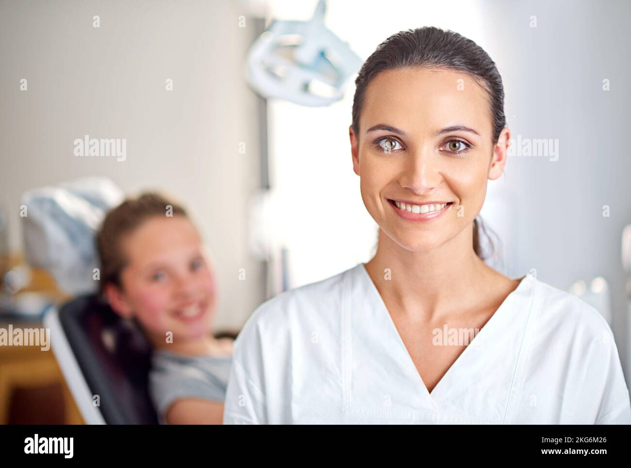 Tutto sui denti. Una dentista femminile in piedi nel suo ufficio con la sua paziente del bambino nello sfondo. Foto Stock