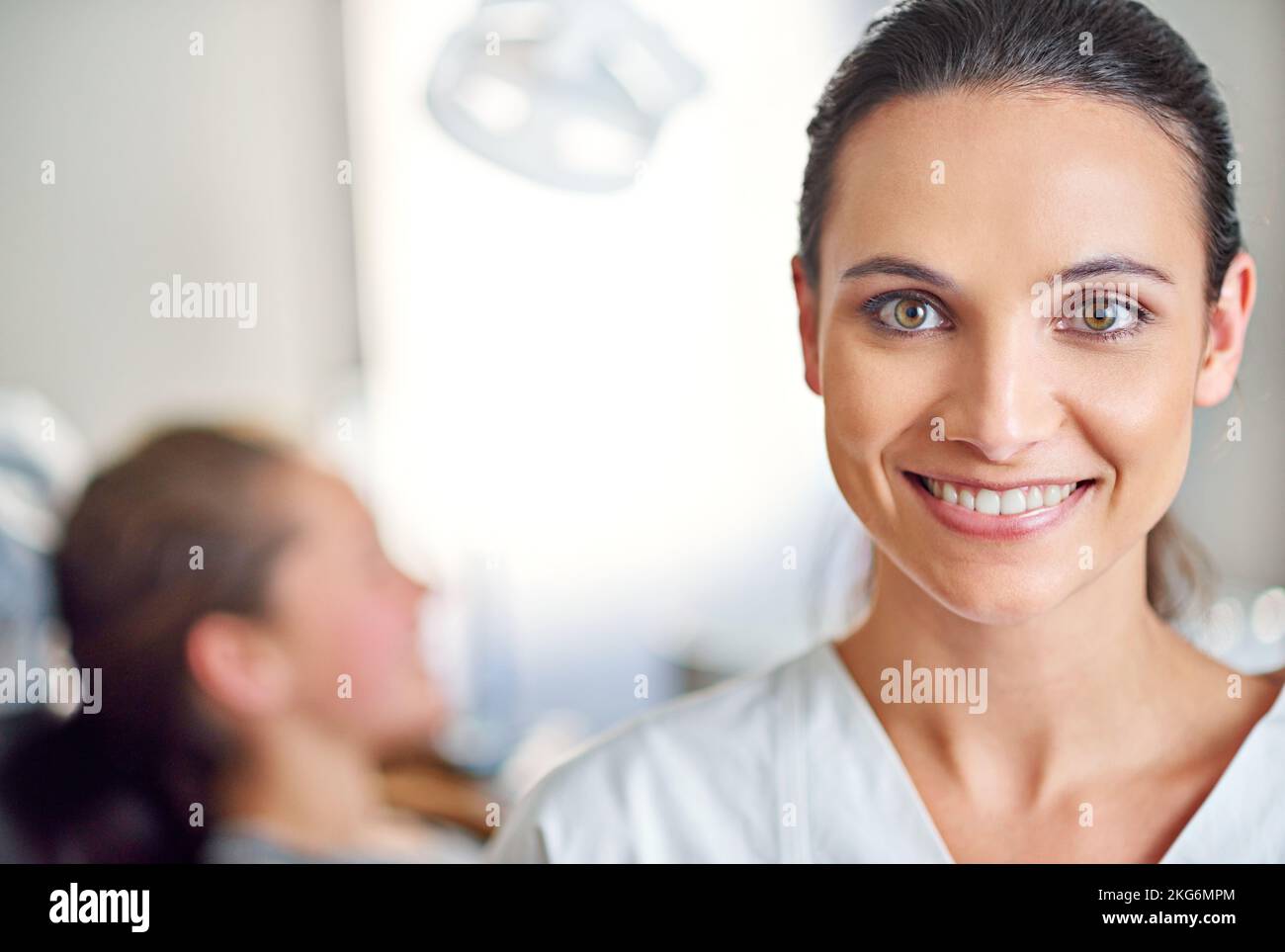 Mi piace quello che faccio. Una dentista femminile in piedi nel suo ufficio con la sua paziente del bambino nello sfondo. Foto Stock