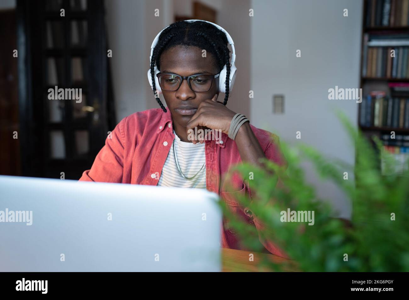 Concentrato di successo afro-americano uomo SVILUPPATORE IT in cuffie è lavora si siede alla scrivania con notebook Foto Stock