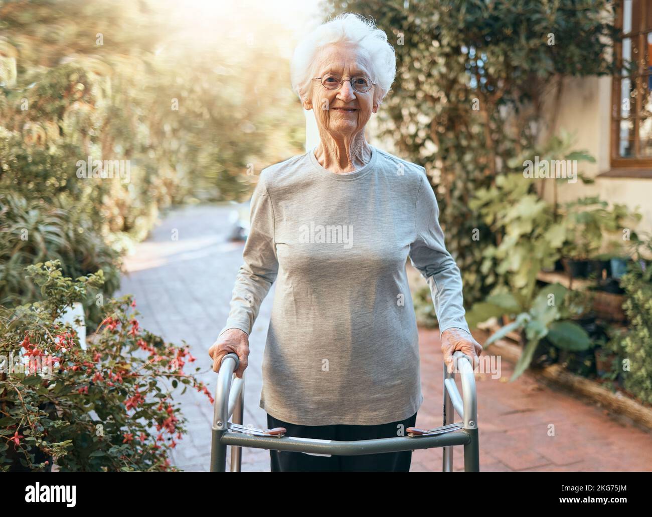 Disabilità, riabilitazione e donna anziana con struttura a piedi per il benessere all'aperto, il corpo in movimento e l'assistenza sanitaria in natura, giardino o parco. Pensionamento Foto Stock
