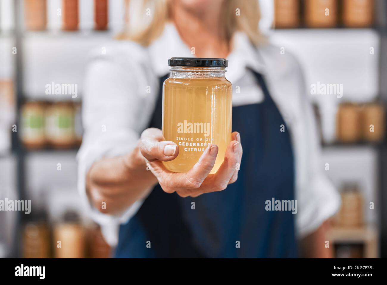 Vetro, miele e mano di donna piccola impresa proprietario che offre prodotto grezzo, biologico e sano nel suo negozio. Affari locali, donna d'affari e miele Foto Stock