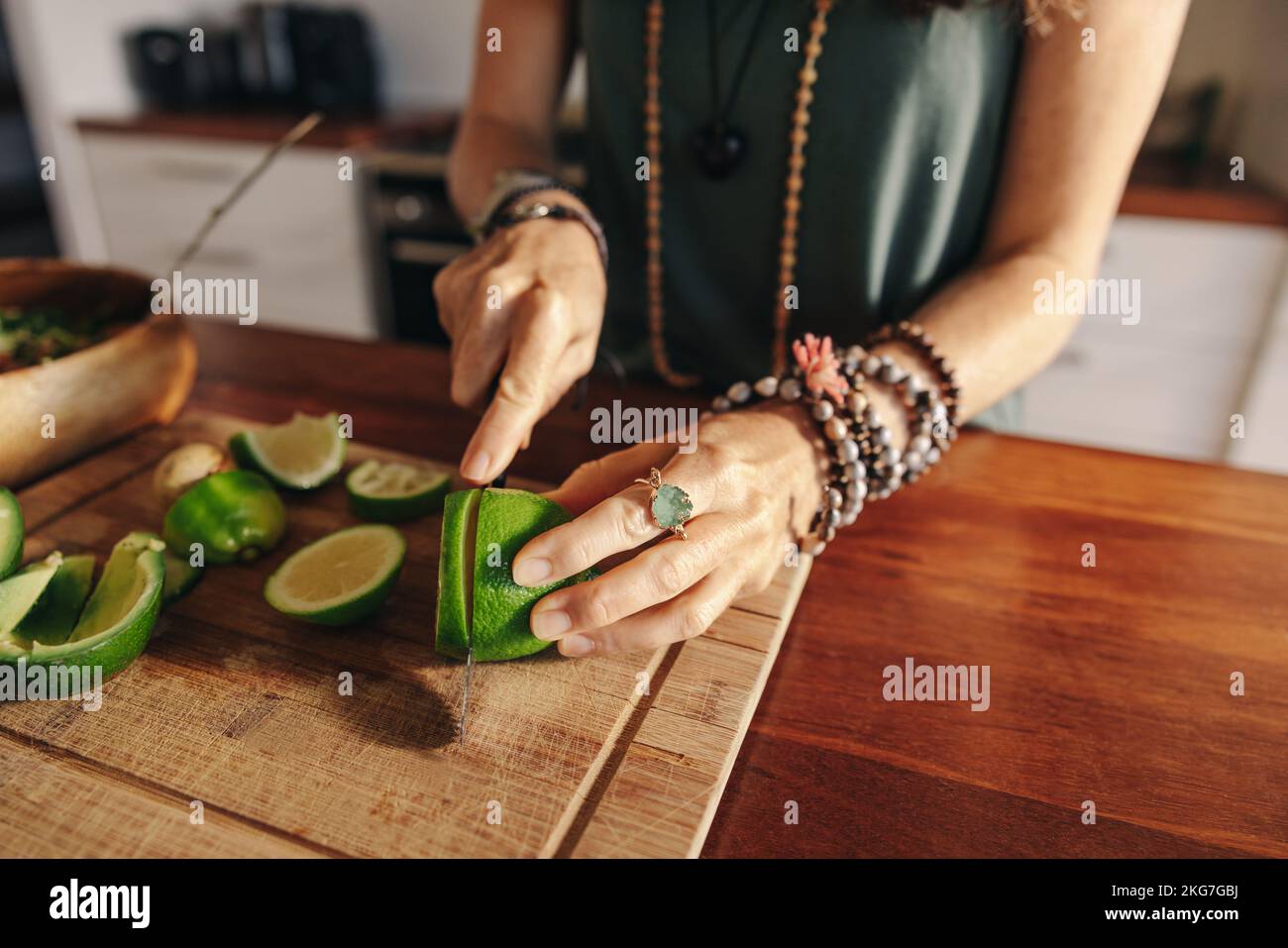 Donna anziana vegetariana che taglia alcuni lime per il succo verde nella sua cucina. Donna matura che prepara un pasto sano a base di piante a casa. Donna che prende l'auto Foto Stock