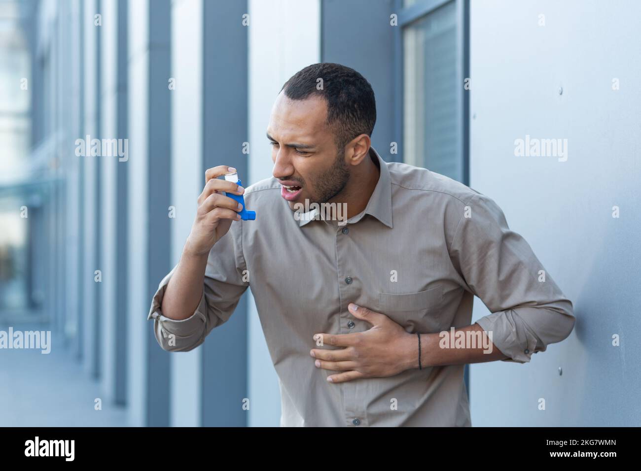 Un attacco di asma, allergie. Un giovane ispanico, afro-americano, sta in piedi fuori usando un inalatore, sperimentando dolore toracico e mancanza di respiro. Ha bisogno di assistenza medica. Foto Stock