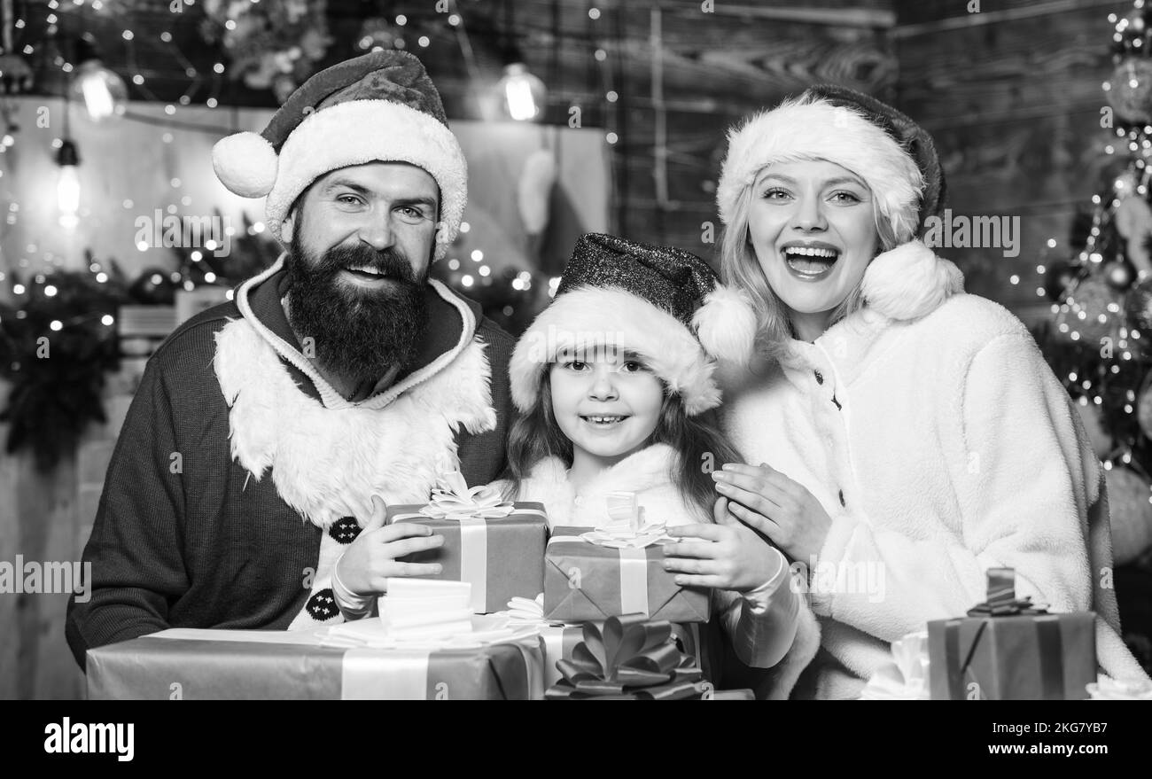 Natale insieme. Il padre e la madre amano la figlia. Scatole regalo di Natale. Regalo aperto. Bambino piccolo e genitori a santa Hat. Vacanze invernali. Shopping Foto Stock