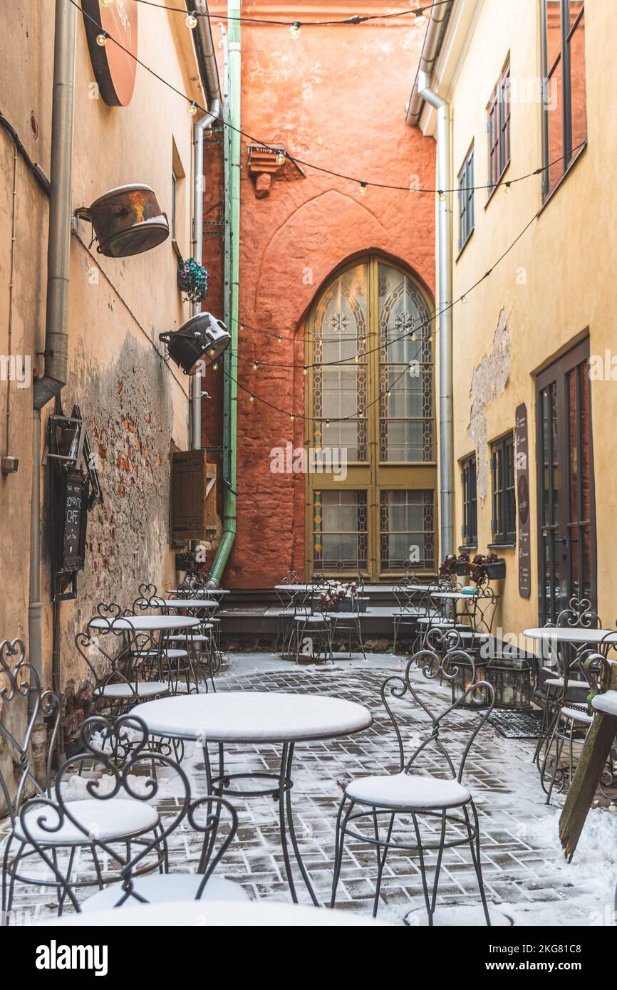 Ingresso con cartello di un accogliente caffè nel centro storico di riga, in Lettonia, in inverno con tavoli e sedie coperti di neve e riflettori vintage, verticale Foto Stock