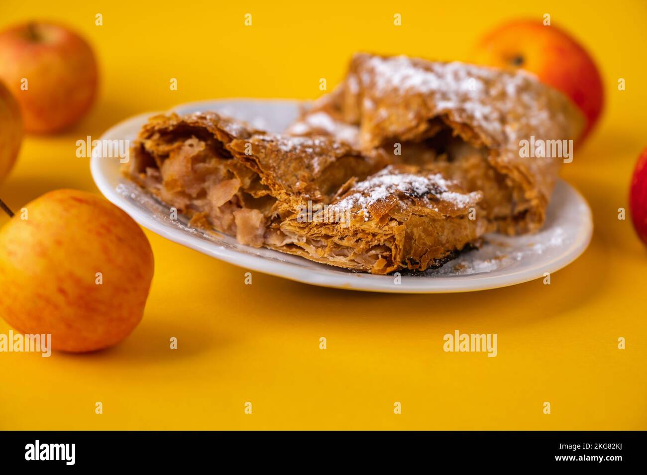 2 pezzo di torta di mele (strudel) su piatto bianco, 4 mela rossa su sfondo giallo, primo piano. Foto Stock