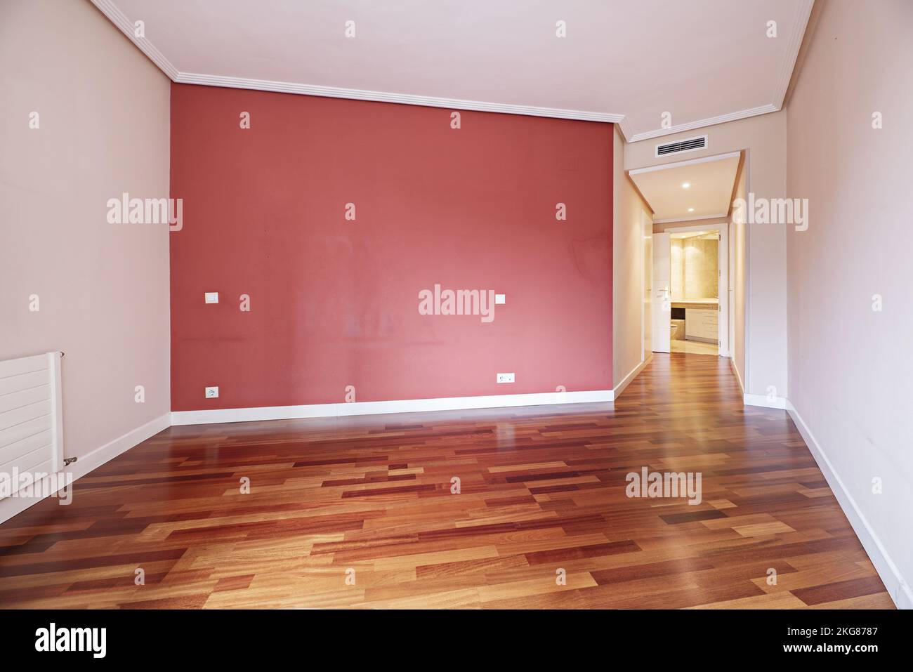 Soggiorno vuoto con pavimento in parquet rossastro con parete dipinta di rosso vino e corridoio con armadi Foto Stock
