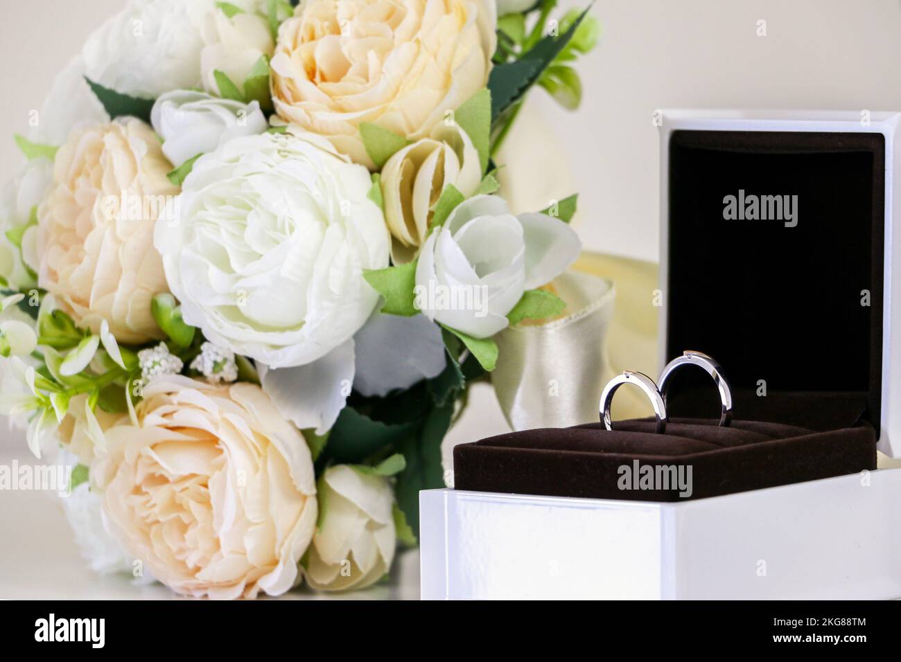 Un paio di squisito lucido suo e suoi anelli di nozze frizzante in ring box oltre al bel bouquet di fiori di nozze, bianco e rose di pesca. Simbolo Foto Stock