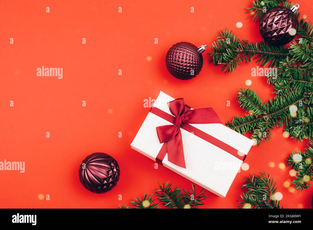 Scatola regalo e rami di abete con decorazioni natalizie su sfondo rosso. Concetto di vacanza invernale. Vista dall'alto, disposizione piatta, spazio di copia Foto Stock