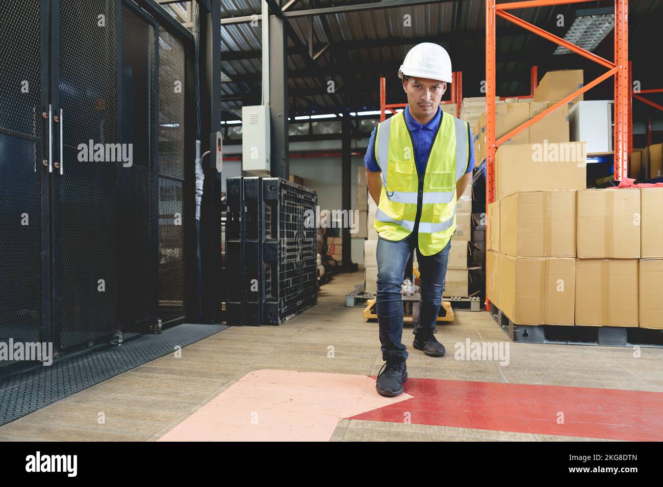 Operatore asiatico di magazzino maschio che tira un transpallet. Lavoratore che lavora con transpallet manuale che scarica le scatole di carico sul pallet nel magazzino. Foto Stock