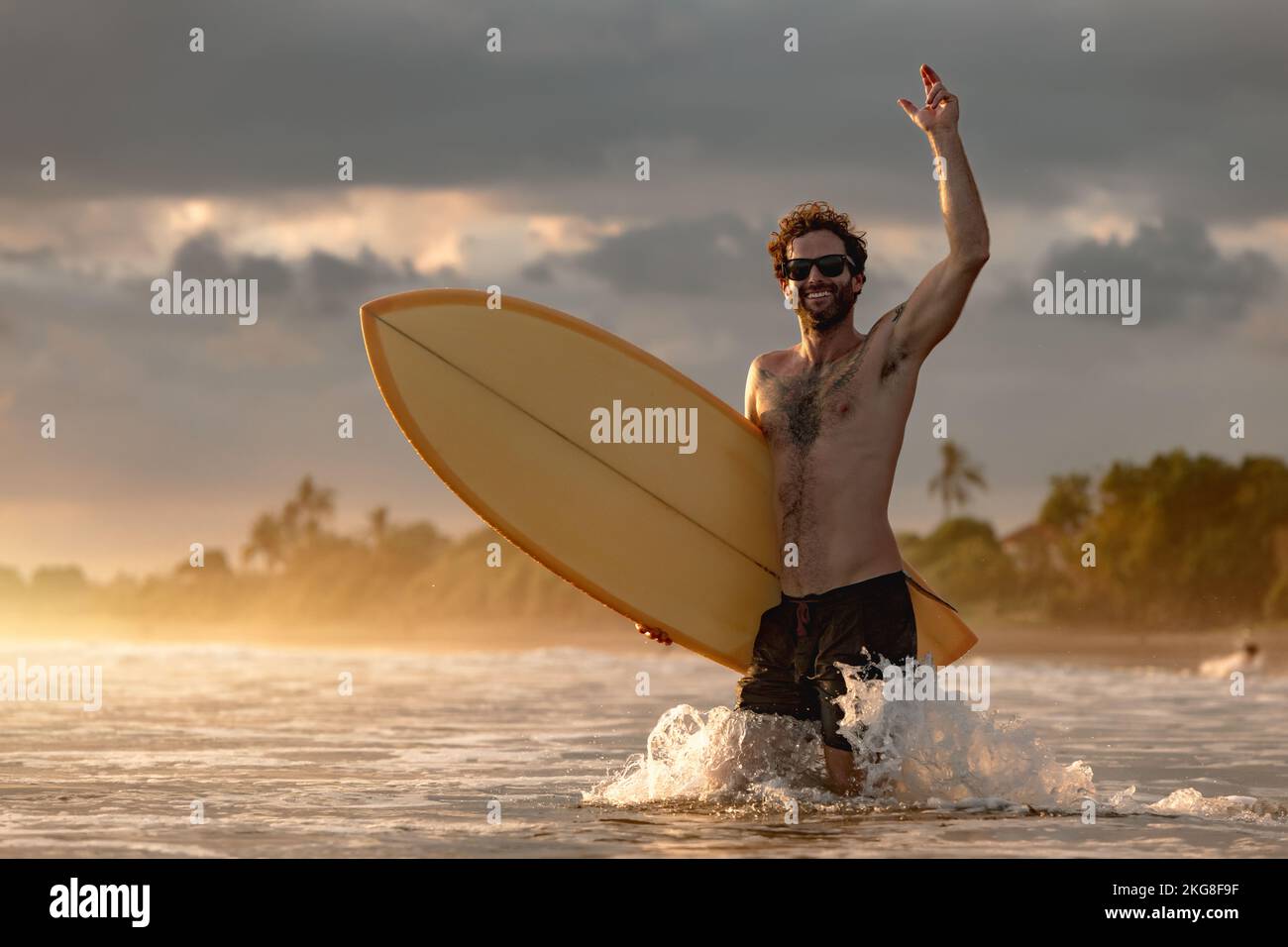 Felice ragazzo attraente surfer va a surfing al tramonto oceano Foto Stock