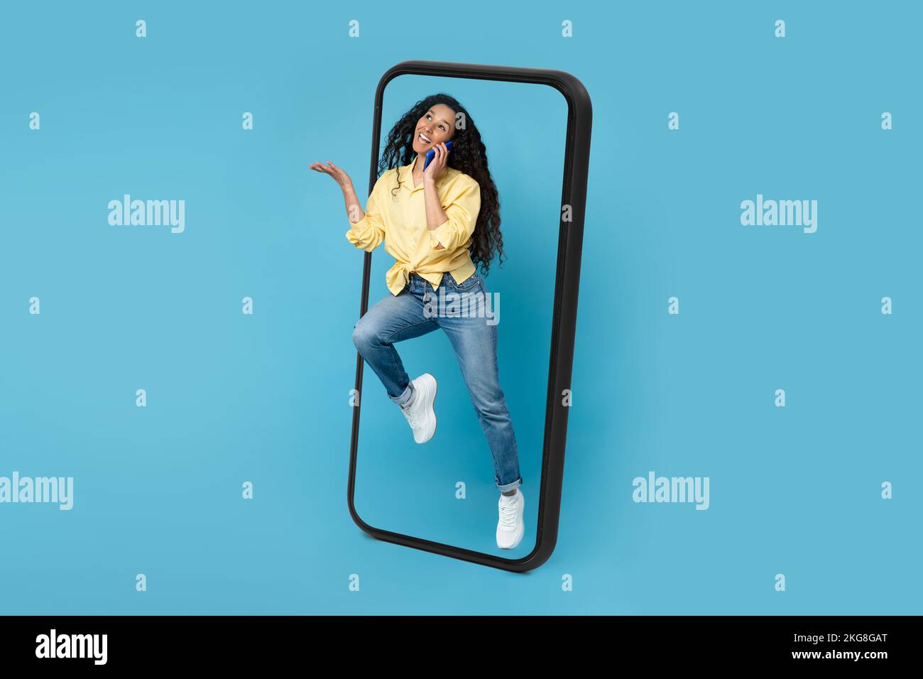 Felice donna araba millennial che chiama da smartphone saltando fuori dall'enorme schermo del telefono Foto Stock
