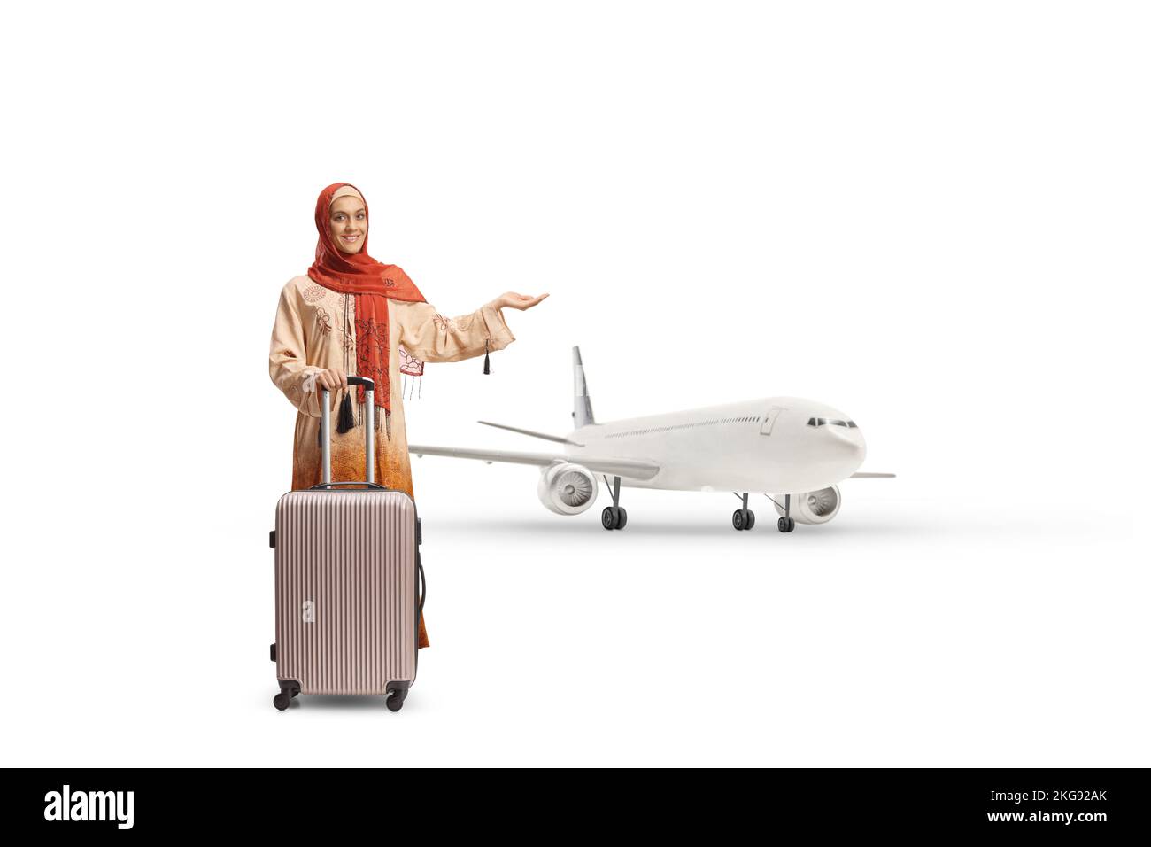 Giovane donna in abiti etnici e hijab con una valigia che indica un aereo isolato su sfondo bianco Foto Stock