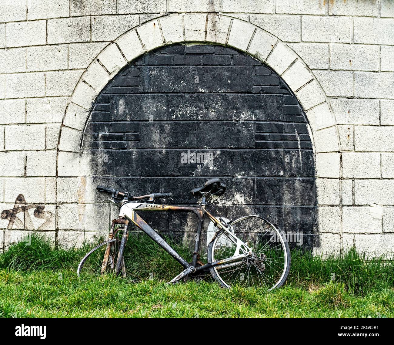 Moto di spinta vandalizzata e bruciata appoggiata al muro Foto Stock