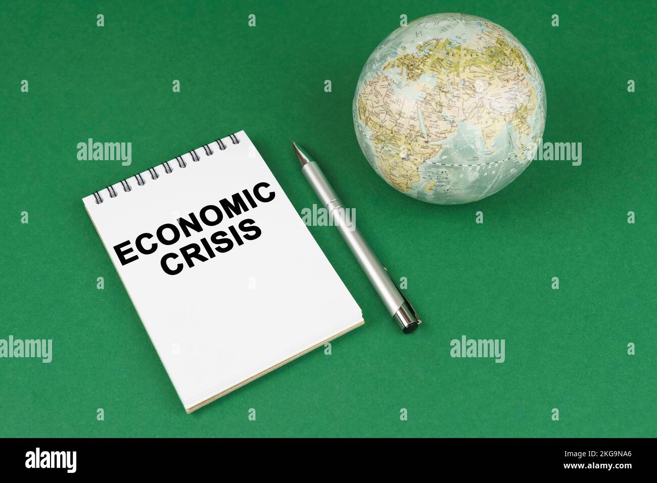Concetto globale. Su una superficie verde si trova un modello del pianeta e un blocco note con l'iscrizione - crisi economica Foto Stock