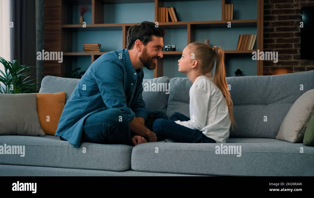 Divertente caucasico giovane famiglia papà e piccola figlia seduta confortevole sul divano amando ragazza carina toccare padre naso divertente scherzo giocare gioco Foto Stock