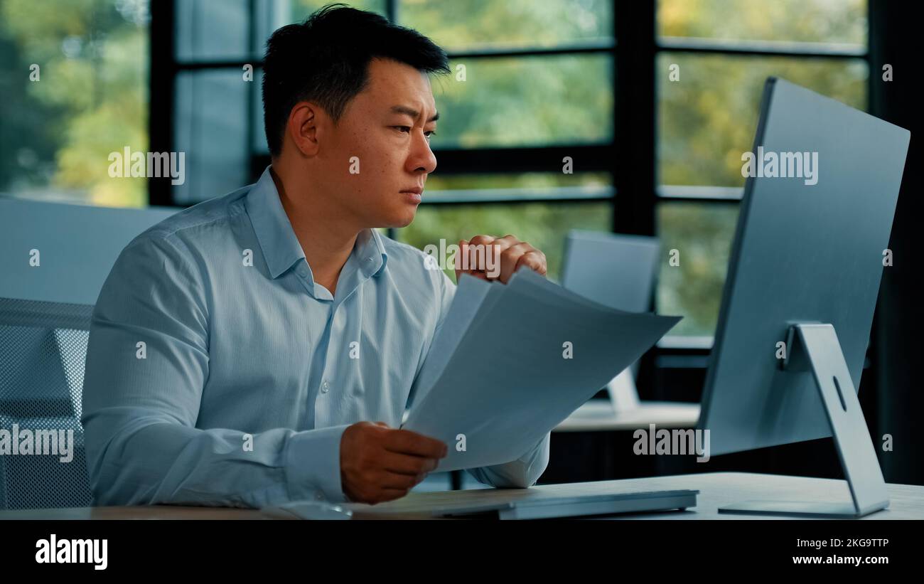 Disperato triste asiatico giapponese senior specialista businessman siede in ufficio leggere documenti truffa errore di notifica nella documentazione commerciale uomo ricerca Foto Stock
