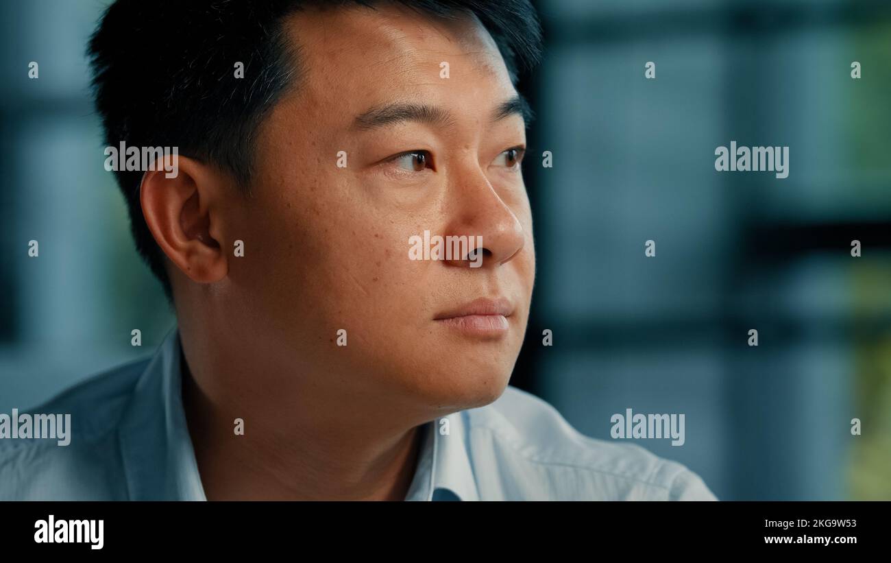 Uomo d'affari datore di lavoro etnico asiatico coreano uomo sedersi da solo in ufficio pensieroso guardando la finestra di pianificazione business idea girare la testa alla fotocamera sorridente Foto Stock