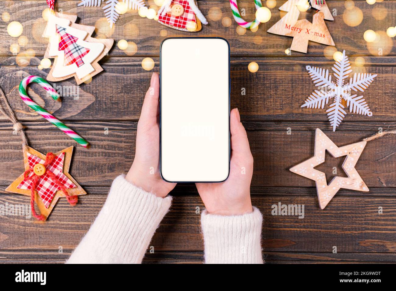 Primo piano donna che tiene il telefono con schermo bianco vuoto mockup vicino decorato albero di festa, festeggiamento di Natale, shopping cliente online, acquisto g Foto Stock