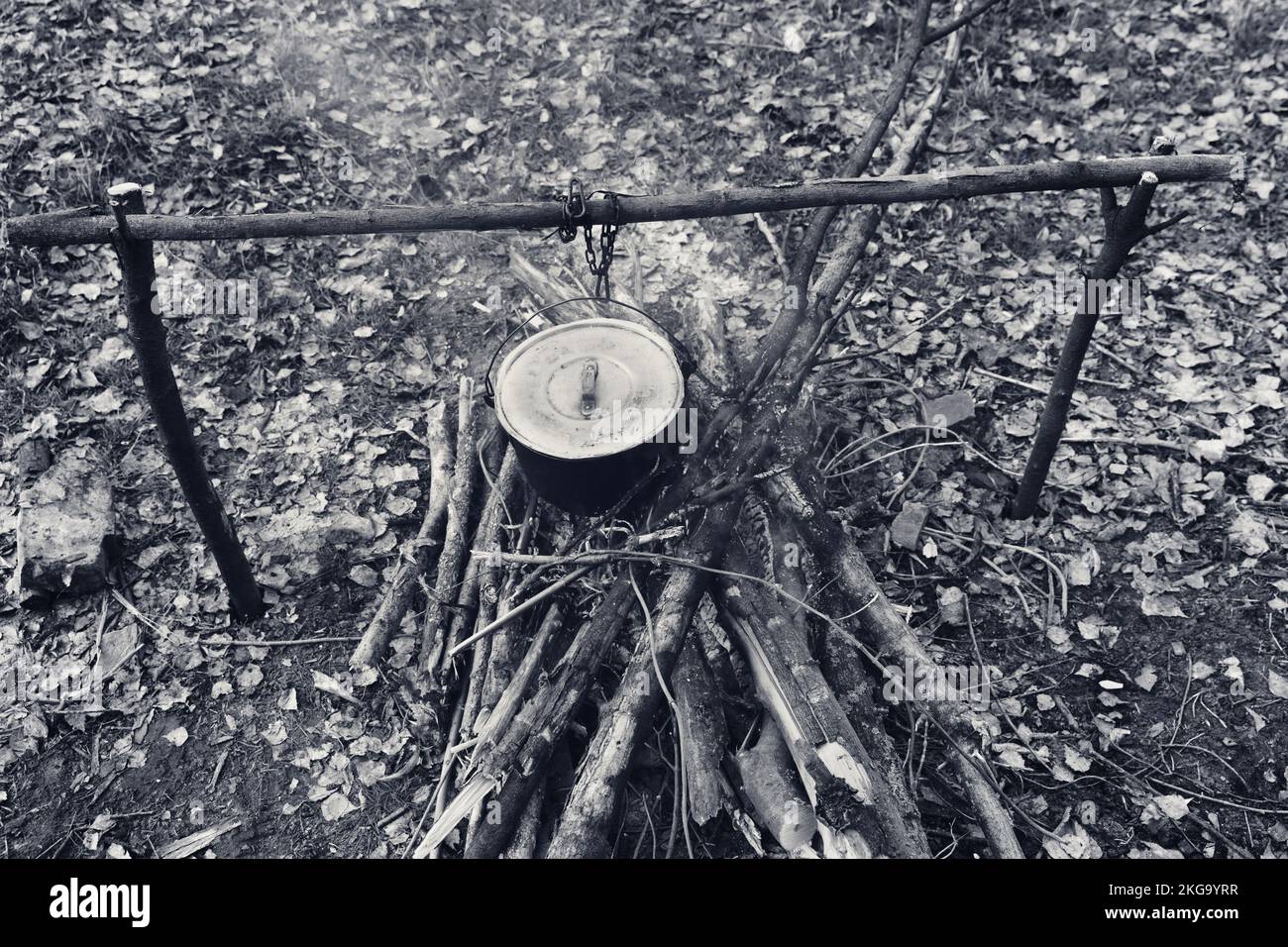Cucinare in vecchio calderone sooty sul fuoco a glade. Vista grandangolare dall'alto. Immagine in bianco e nero con tonalità retrò. Foto Stock