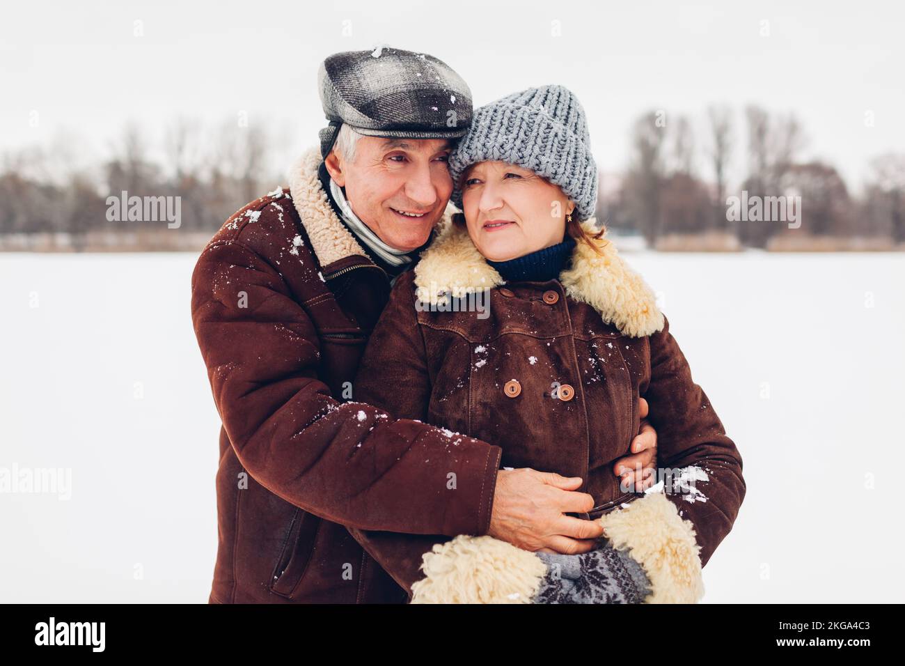 Ritratto di coppia di famiglia anziana che cammina all'aperto durante il tempo nevoso invernale. Persone mature che abbraccia Foto Stock