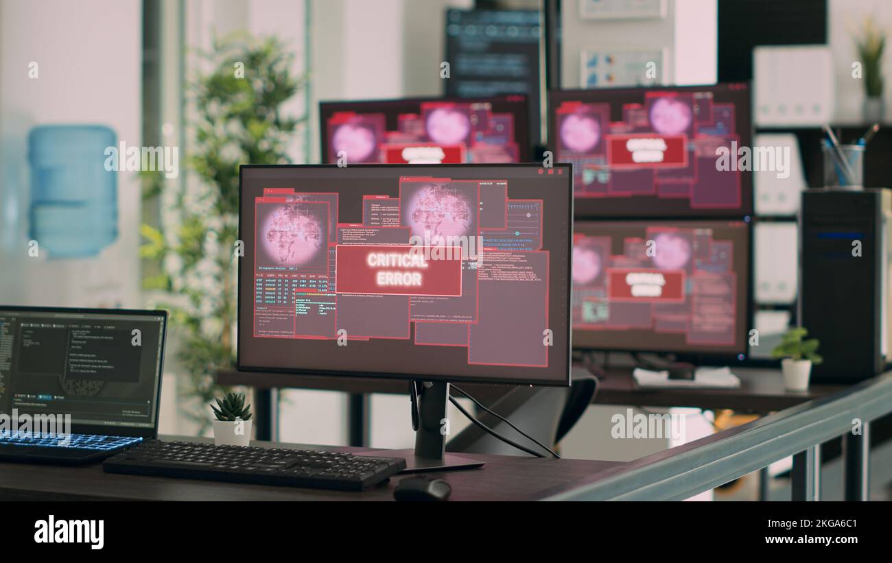 Svuotare la scrivania dell'ufficio IT con più computer che mostrano un avviso di violazione della sicurezza sull'app di rete. I monitor visualizzano un messaggio di errore critico lampeggiante sullo schermo con un avviso di arresto anomalo del sistema. Foto Stock