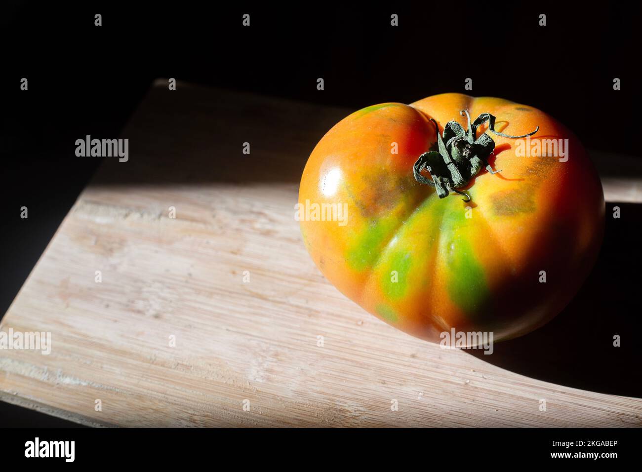 Vista dall'alto del grande pomodoro rosso succoso con verde in contrasto con la luce del sole di Rembrandt. Vegetale isolato su superficie di legno con fondo nero. Biologico Foto Stock