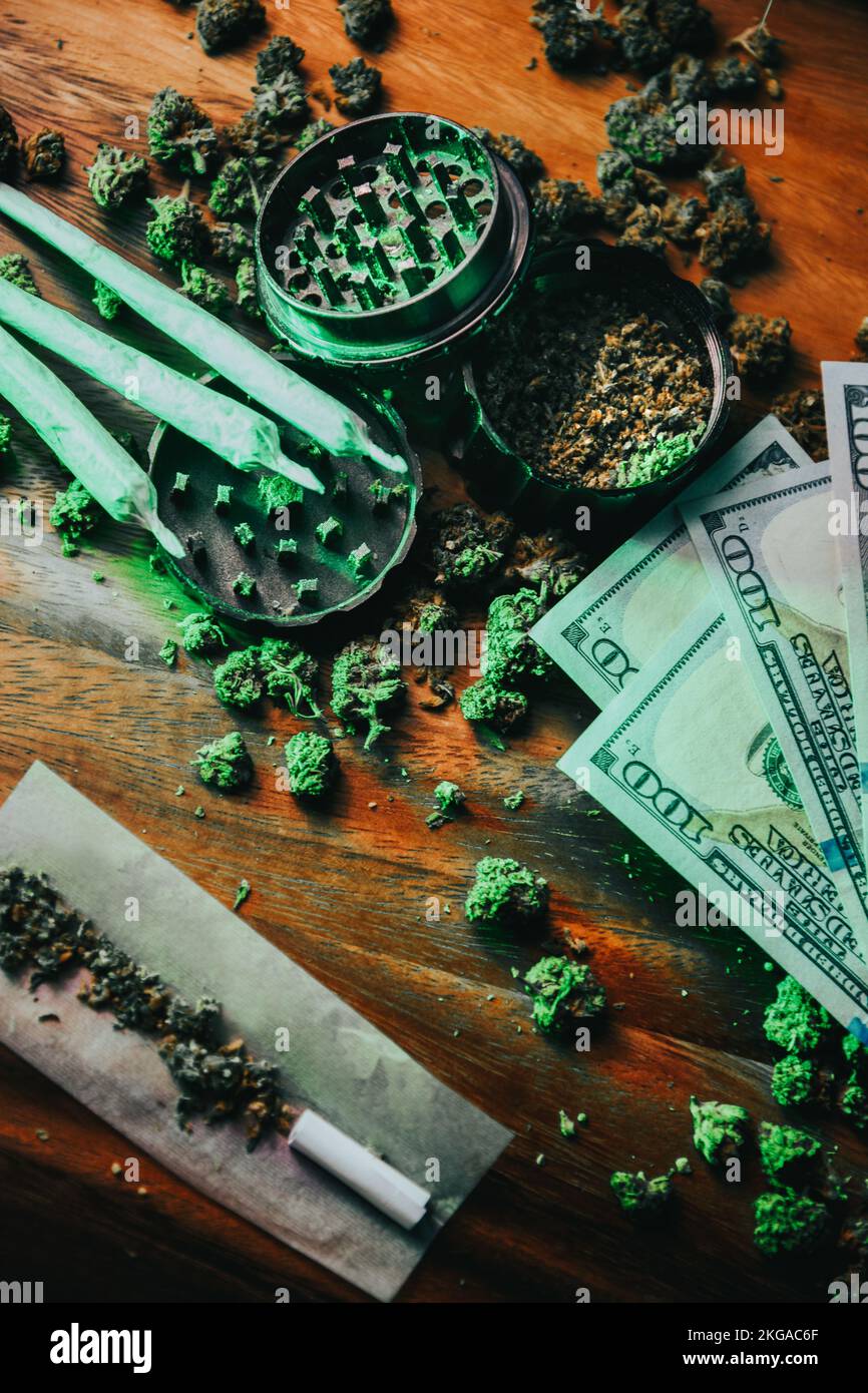 Boccioli di marijuana con droghe, cbd e thc. Smerigliatrice e giunti. Carta comune, filtri per sigarette, denaro. Affari sporchi, casa del concessionario. Droghe e dipendenza, Foto Stock