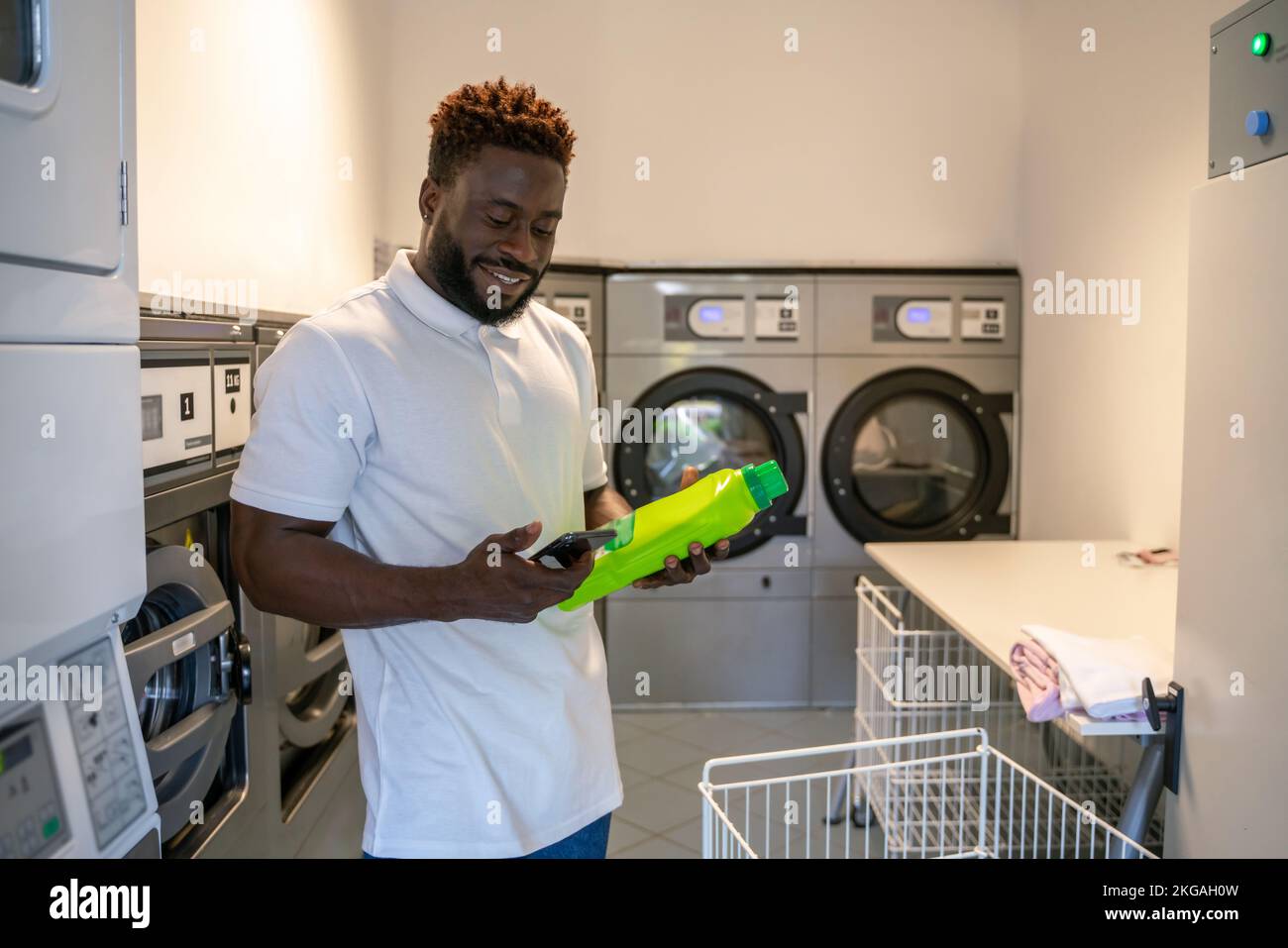 Felice giovane uomo in piedi ad una lavanderia self-service Foto Stock
