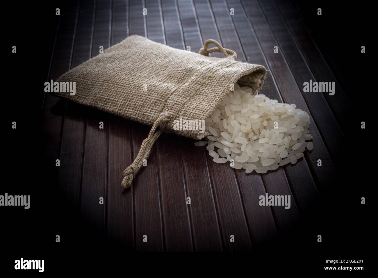Una sacca di paglia pieno di riso crudo su uno sfondo di legno Foto Stock